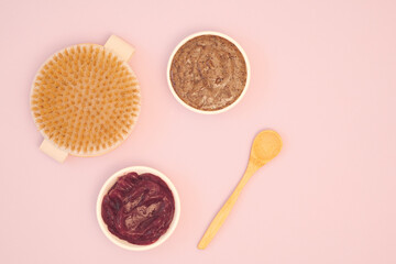 Home body skin care concept. Natural homemade scrub, fruit cream, dry body massage brush and wooden spoon on a pink background. Copy space, flat lay, top view