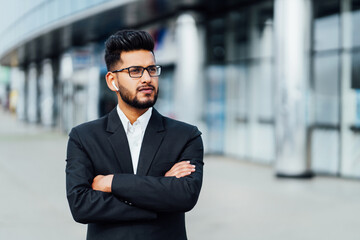 Fototapeta premium A modern Indian office worker, a bearded handsome Indian man, behind him a modern office building