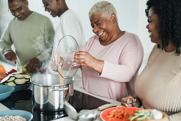 Happy black family cooking inside kitchen at home - Father, daughter, son and mother having fun preparing lunch - Main focus on mum face