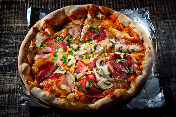 Round pizza on a wooden board. Pizza on a black table close up. Contrasting dramatic light as an artistic effect.