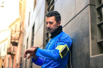 Male using fitness app on smartphone. Man resting after jogging reading run results. Runner with mobile phone connected to a smart watch recording data of sport activity checking wearable technology