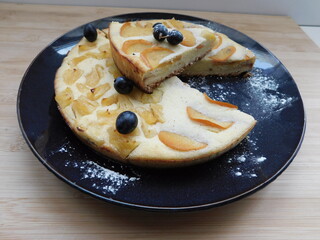 cheesecake on a black plate on a wooden table, decorated with grapes.