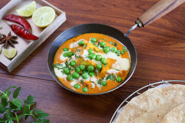 Matar Paneer curry, paneer butter masala recipe made using cottage cheese, green peas, served in a bowl. Delhi, Rajasthan India. Indian veg curry wooden background. side dish of Roti, Chapati, naan