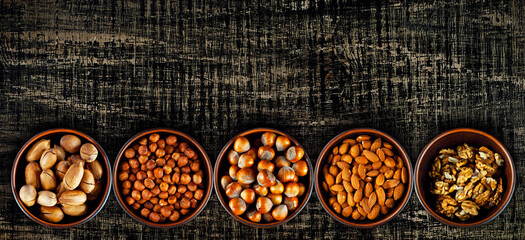 Cashews, hazelnuts, almonds, walnuts, pecans close up. Nuts in a clay bowl on a brown board. Nuts on an old shabby table. Copy space and free space of text. Mockup.