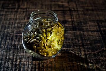 Peeled pumpkin seeds in a glass jar on a wooden table. Seeds on a black shabby board. Copy space...