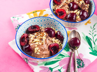 Chocolate ice cream with sprinkles, nuts and fresh cherries on pink napkin