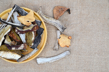 Dried red and porcini mushrooms on a wooden plate. Some of the mushrooms are scattered around.