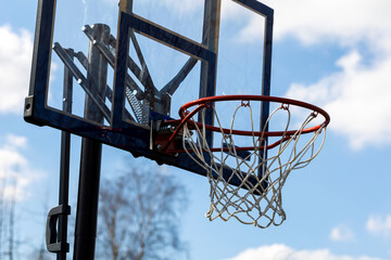 A portrait of a recreational outdoor basketball rim with a net and a plexiglass backboard with blue...
