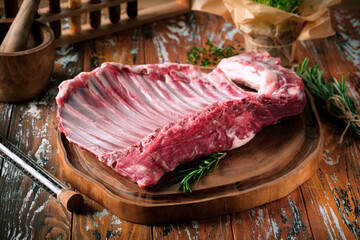 Young lamb ribs on a wooden board with seasonings and herbs. Raw meat for bone-in steaks © Andrey