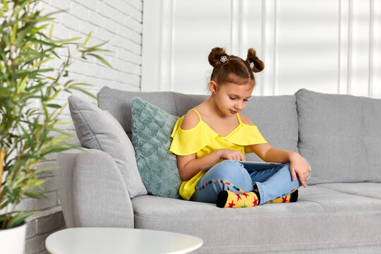 little child girl using digital tablet on sofa at home. kid enjoying tablet