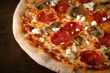Spicy pepperoni pizza with sausage, mushrooms and goat cheese. Cooked pizza on a wooden table, close up