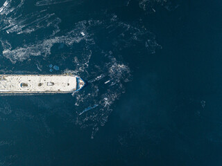 Obraz premium The barge floats on the freezing river. Aerial drone view. Sunny winter day, thin ice on the river.