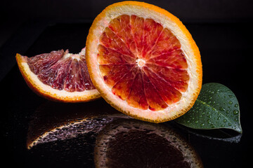 Red sicilian orange fruit cut on two and green leaf on black reflective background. Fresh, ripe bloody orange wallpaper