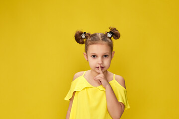 cute little child girl showing silence gesture on yellow studio background. kid holding finger on...