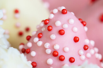 A close-up view of pink chocolate candy sprinkled with red and white balls, selected focus. Delicious sweets and desserts.