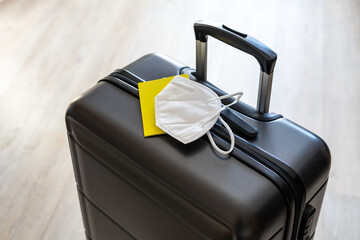 Ein grauer Reisekoffer, ein gelber Impfpass und eine weiße FFP2 Maske. Reise, Urlaub, Corona...