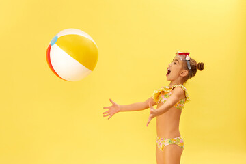 cute little child girl in swimwear playing with beach ball on yellow background