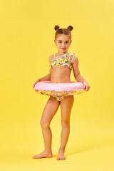 cute little child girl in swimwear with inflatable rubber ring on yellow background