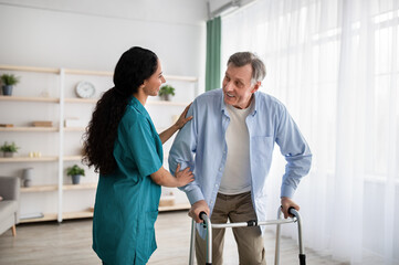 Young nurse helping older man to walk with frame at retirement home. Professional eldercare service
