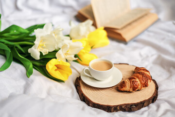 Fototapeta na wymiar Breakfast in bed. A bouquet of tulips lies on the bed next to a cup of hot coffee. Spring. Gift. Good morning.