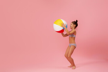 child girl in swimwear playing with beach ball on pink background. summer time