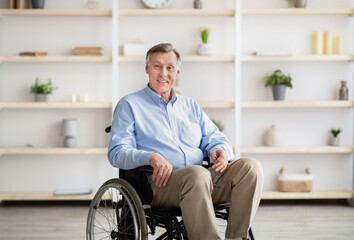 Joyful handicapped senior man in wheelchair smiling and looking at camera at retirement home