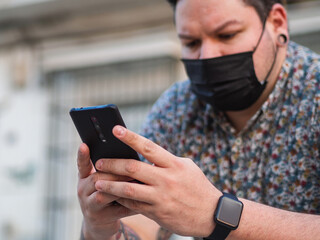 Hombre joven usando su teléfono móvil en la calle con una mascarilla sanitaria para la pandemia del coronavirus