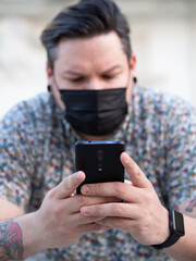 Hombre joven usando su teléfono móvil en la calle con una mascarilla sanitaria para la pandemia del coronavirus