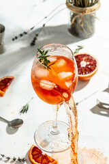 Ice cubes breaking wine glass filled with Aperol Spritz cocktail on white background.