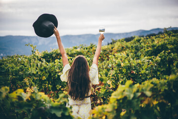  Woman relaxing in the vineyards. Woman holding glass with white wine. - obrazy, fototapety, plakaty