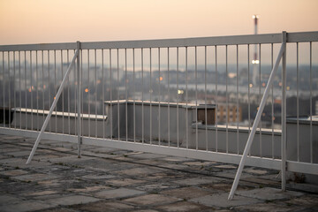 Safety fence on skyscraper rooftop with city background at sunset, shallow depth of field. Roof top balcony with cityscape.