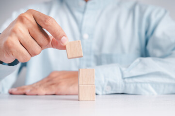 Businessman wearing a blue shirt, arranging the empty wooden blocks with his hands. Which is placed on a white wooden table. Business strategy and action plan. Copy space.