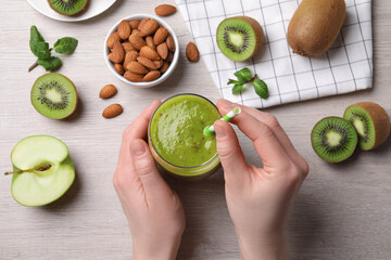 Woman with delicious kiwi smoothie and ingredients at white wooden table, top view