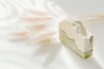 Handmade soap and dried bunny tail grass. Sunshade shadow on white background. Zero waste, eco friendly cosmetics concept. Vintage color filter.