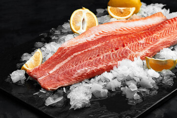 Lightly salted trout. Fresh fish fillet with culinary ingredients, herbs and lemon on a black background, side view
