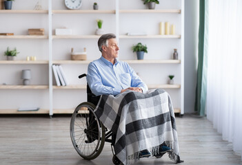 Sad disabled senior man sitting on wheelchair alone at retirement home, looking through window