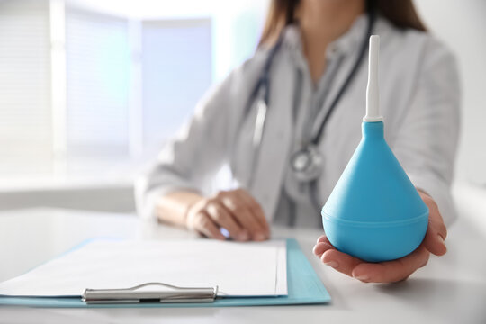 Doctor holding light blue enema at table in hospital, closeup