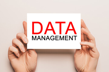 Female hands hold card paper with text DATA MANAGEMENT on a yellow background. Business and finance concept