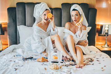 Woman wearing bathrobe sitting on bed and having fun with fruit.
