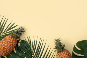 Top view of fresh pineapple with tropical leaves on yellow background.