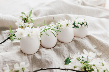 Obraz na płótnie Canvas Natural easter eggs in floral crowns on linen fabric with blooming spring branch and white petals