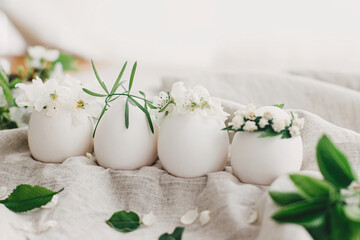 Natural easter eggs in floral crowns on linen fabric with blooming spring branch and white petals