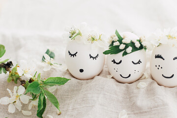 Happy Easter! Natural eggs with drawn cute faces in floral wreaths on linen fabric with bloom