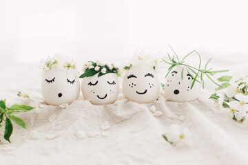 Happy Easter! Natural eggs with drawn cute faces in floral wreaths on linen fabric with bloom