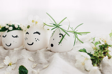 Easter eggs with drawn funny faces in floral wreaths on linen fabric with bloom. Happy Easter