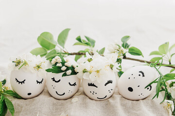 Happy Easter! Natural eggs with drawn cute faces in floral wreaths on linen fabric with bloom