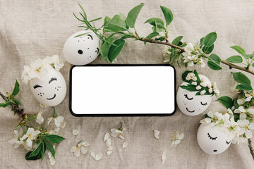Phone with blank screen on rustic background of easter eggs with drawn cute faces in floral wreaths
