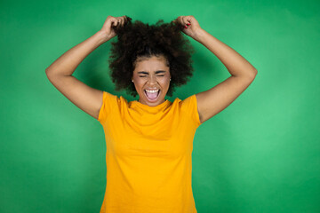 African american woman wearing orange casual shirt over green background suffering from headache desperate and stressed because pain and migraine with her hands on head