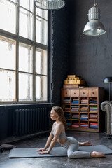 Young beautiful woman in a sport suit doing stretching exercises in a loft apartment. Sports during a pandemic on isolation, online gymnastics and yoga classes. Healthy lifestyle. Vertical photo