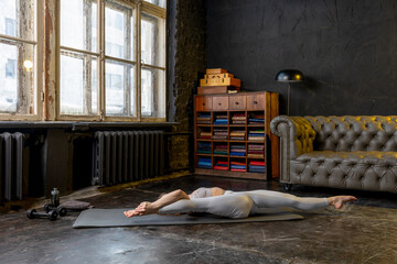 Young beautiful woman in a sport suit doing stretching exercises in a loft apartment. Sports during a pandemic on isolation, online gymnastics and yoga classes. Healthy lifestyle
